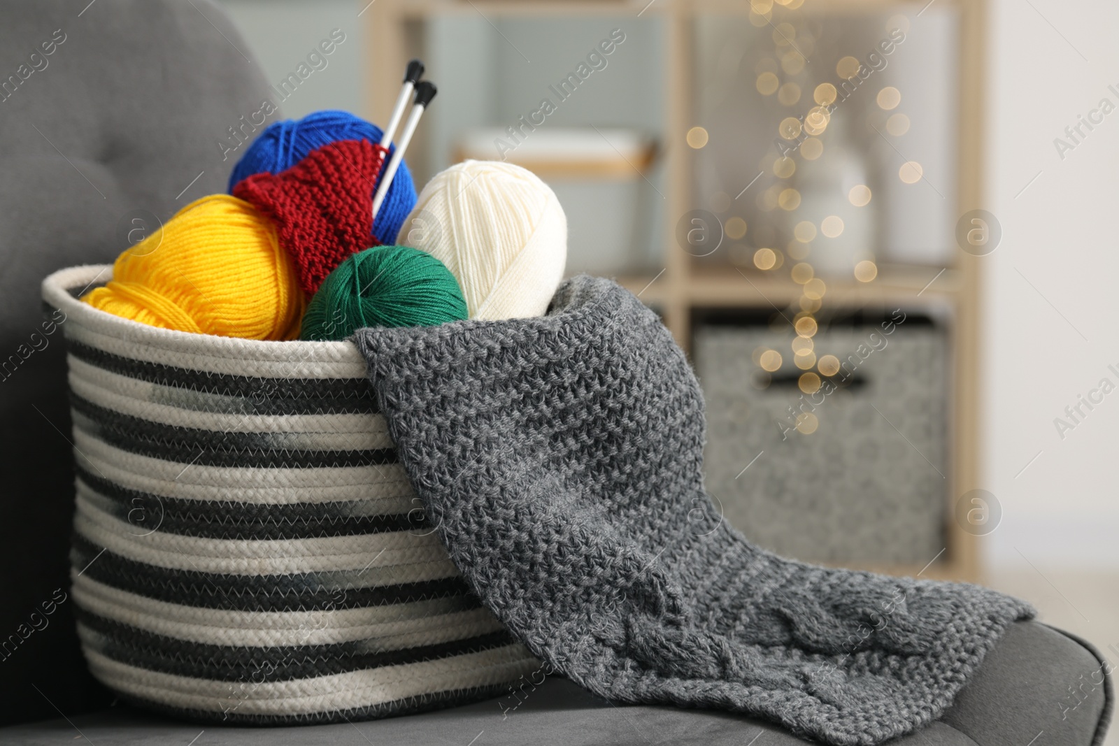 Photo of Skeins of soft yarn, knitting sample and needles on armchair indoors