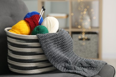 Skeins of soft yarn, knitting sample and needles on armchair indoors