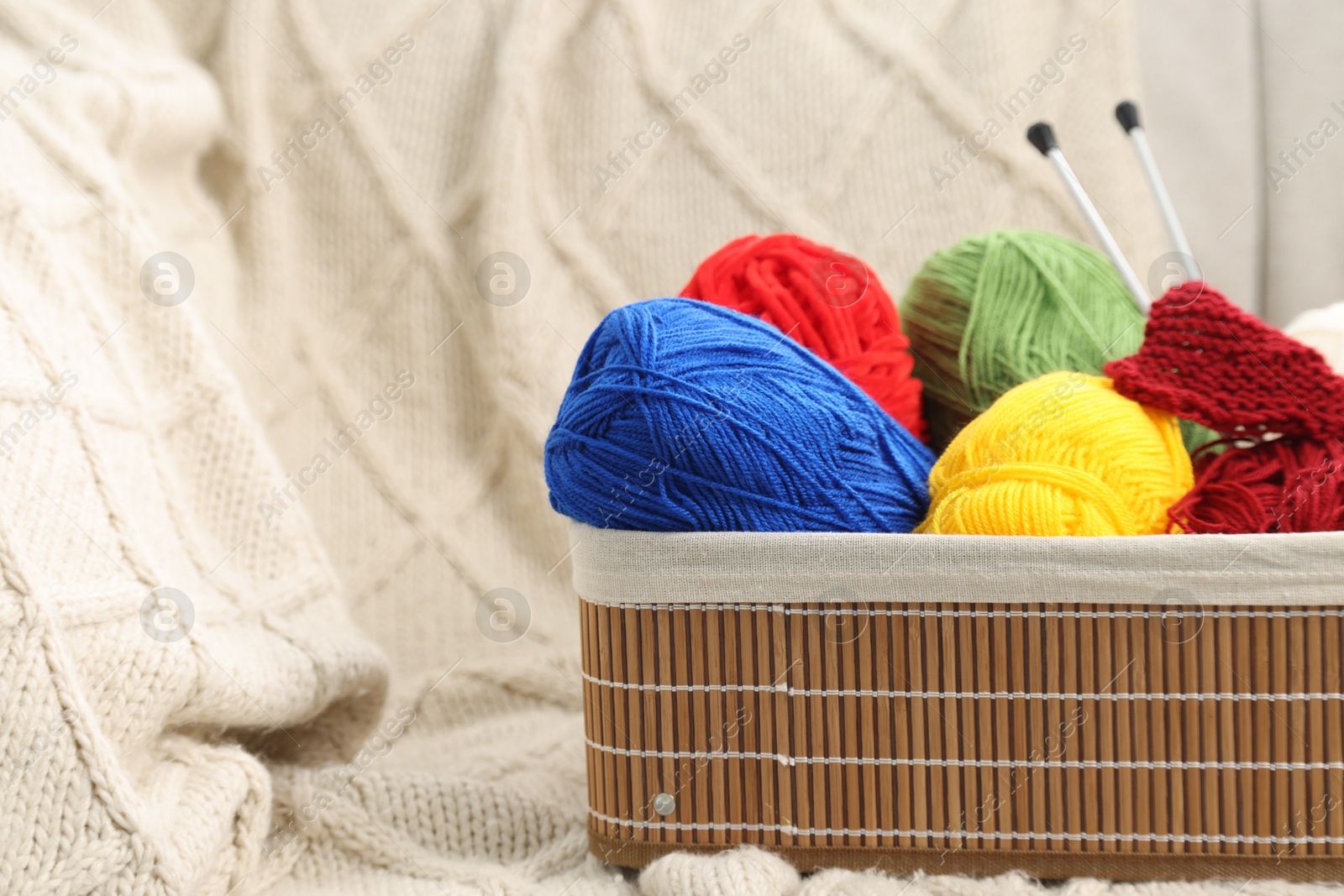 Photo of Skeins of soft yarn, knitting sample and needles in crate on plaid