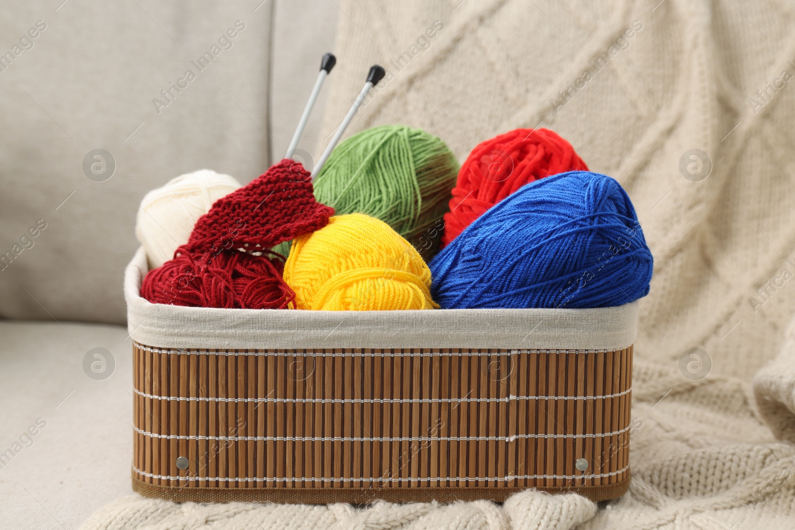 Photo of Skeins of soft yarn, knitting sample and needles in crate on sofa