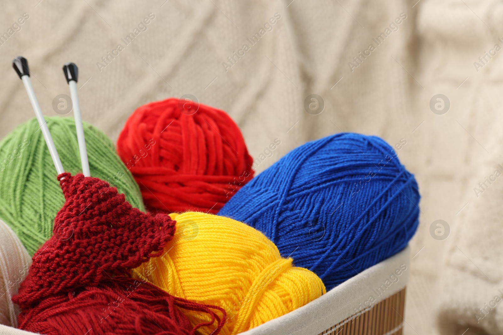 Photo of Skeins of soft yarn, knitting sample and needles in crate indoors, closeup