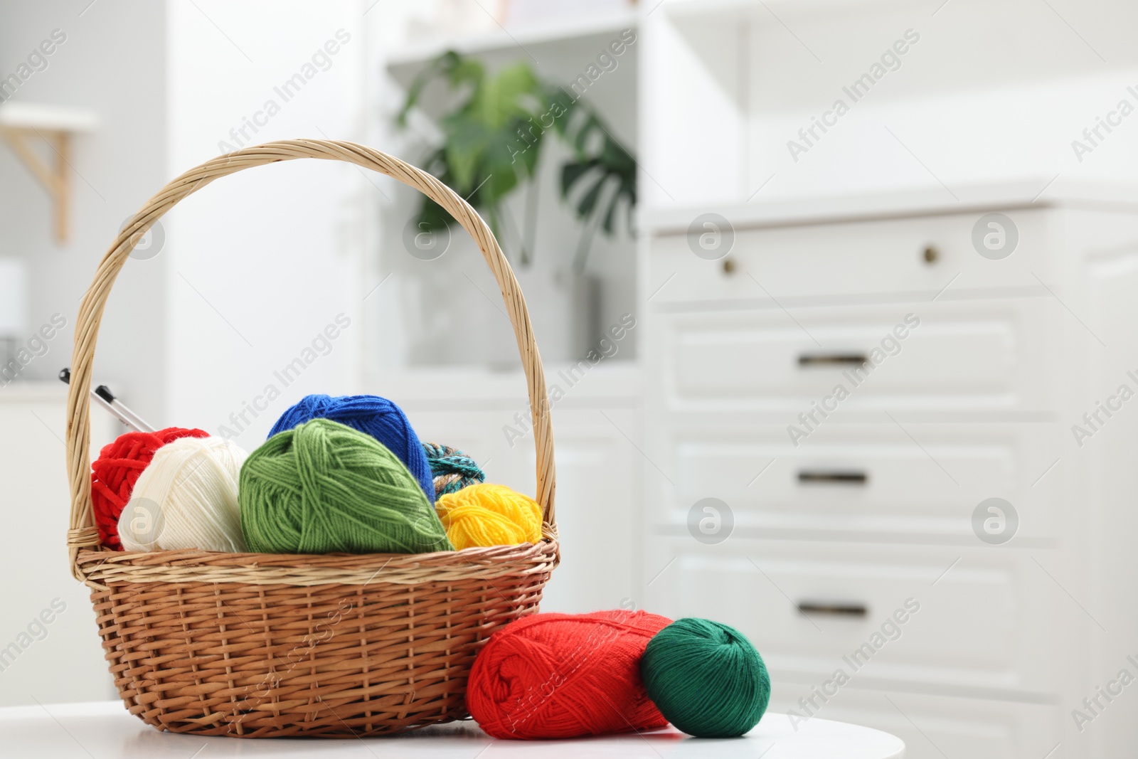 Photo of Skeins of soft yarn and knitting needles on white table indoors. Space for text