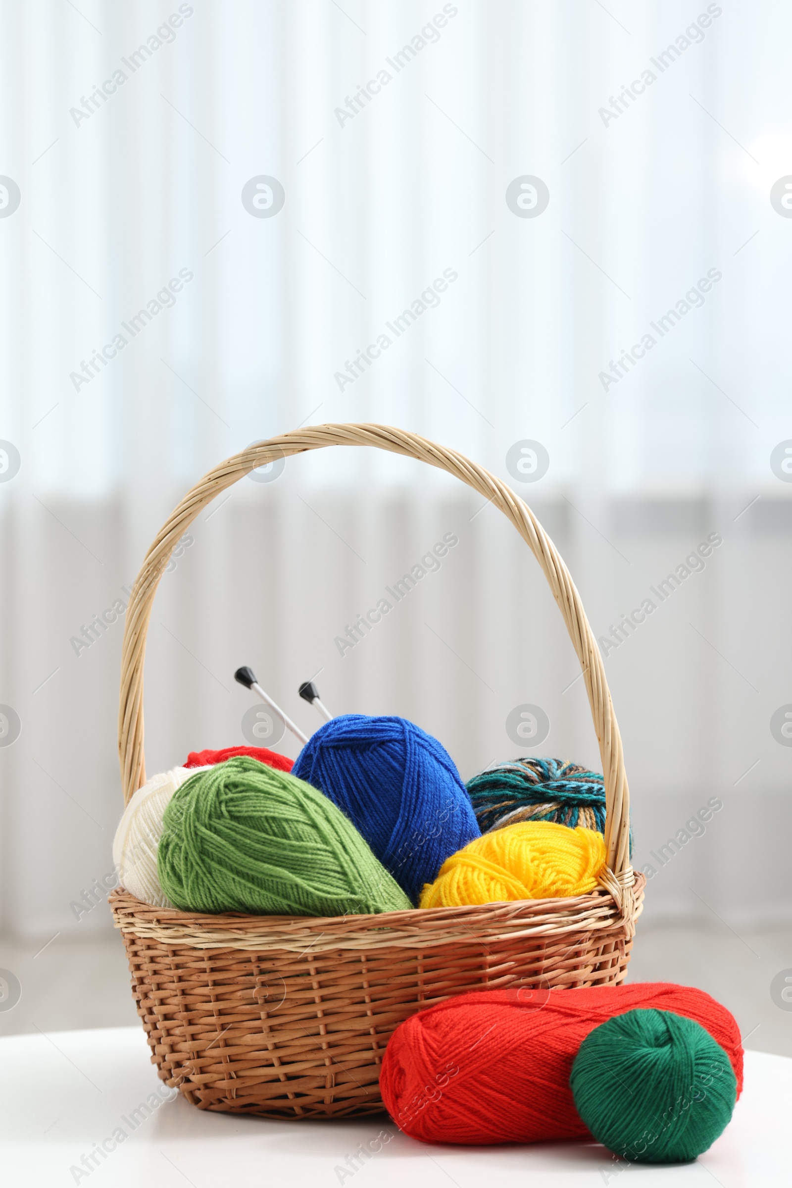 Photo of Skeins of soft yarn and knitting needles on white table indoors