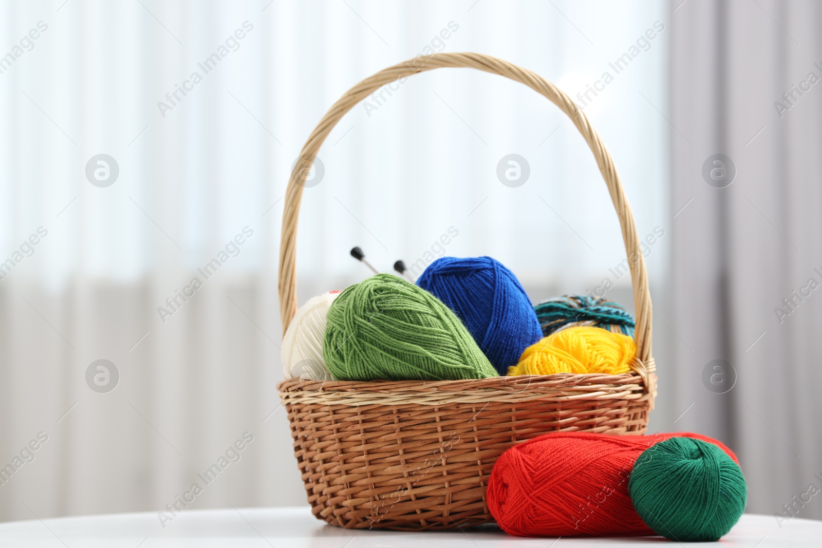 Photo of Skeins of soft yarn and knitting needles on white table indoors