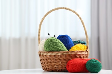 Photo of Skeins of soft yarn and knitting needles on white table indoors