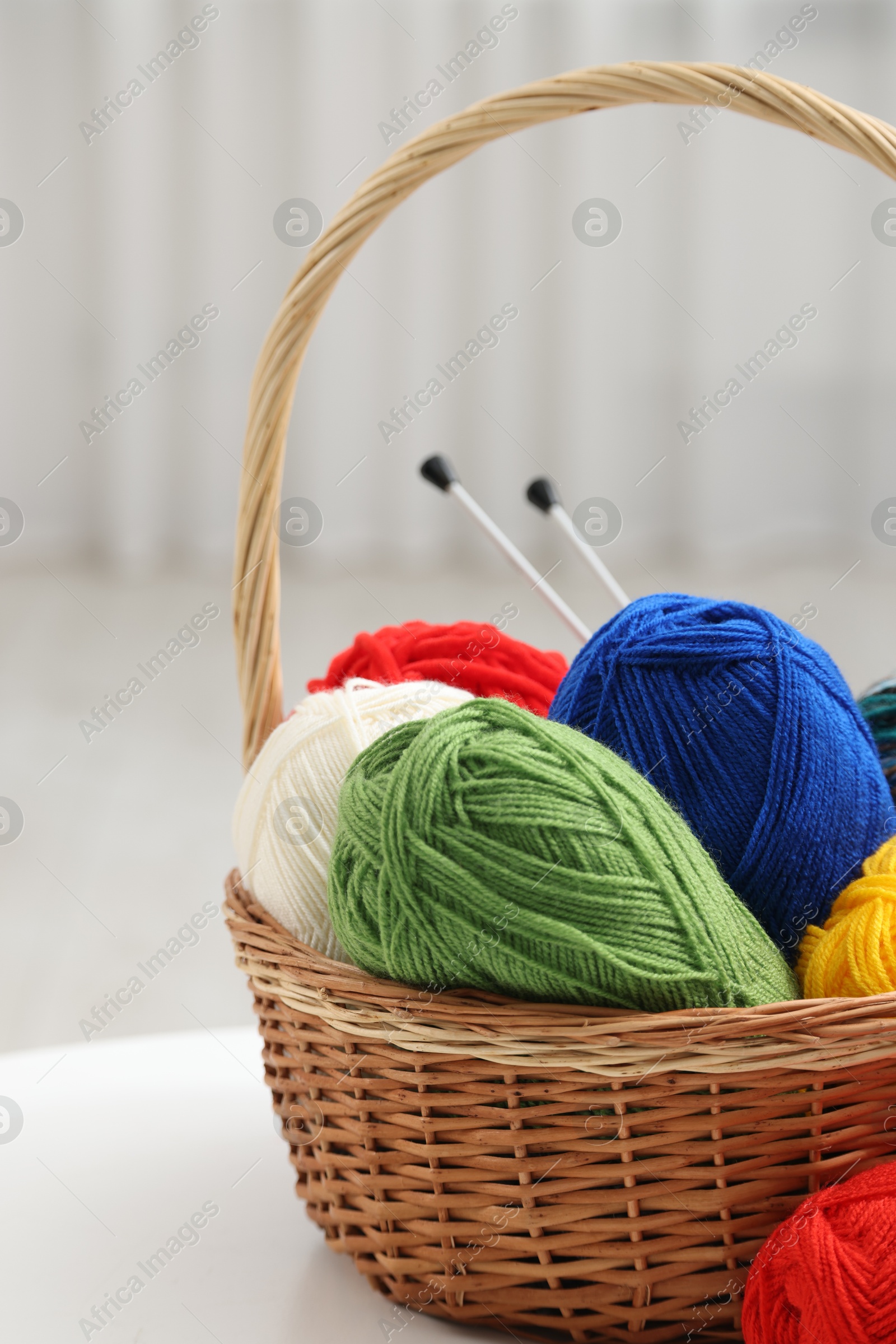 Photo of Skeins of soft yarn and knitting needles on white table indoors, closeup