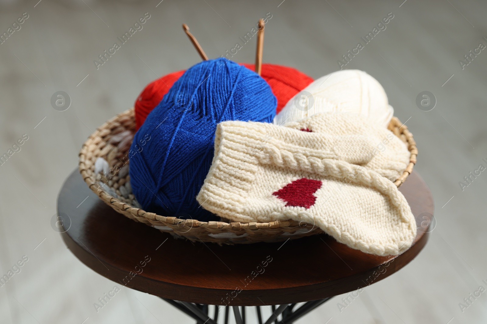 Photo of Skeins of soft yarn, crochet hooks and mittens on coffee table indoors