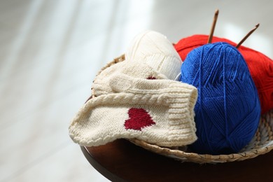 Photo of Skeins of soft yarn, crochet hooks and mittens on coffee table indoors