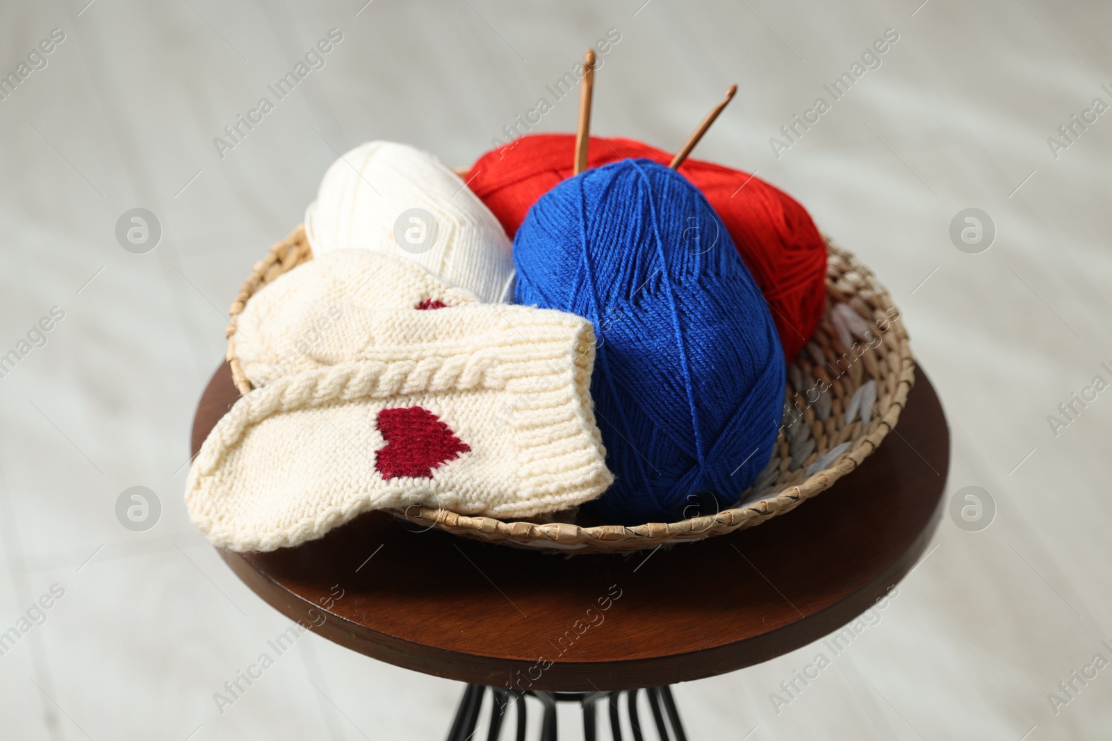 Photo of Skeins of soft yarn, crochet hooks and mittens on coffee table indoors