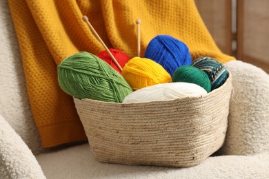 Skeins of soft yarn and knitting needles on armchair