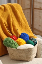 Skeins of soft yarn and knitting needles on armchair indoors