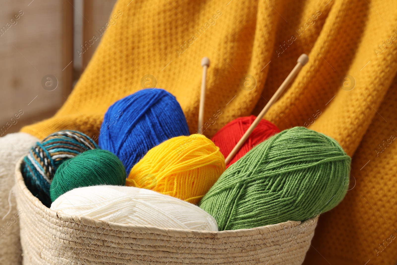 Photo of Skeins of soft yarn and knitting needles on armchair, closeup