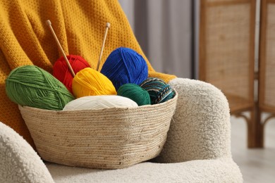 Skeins of soft yarn and knitting needles on armchair