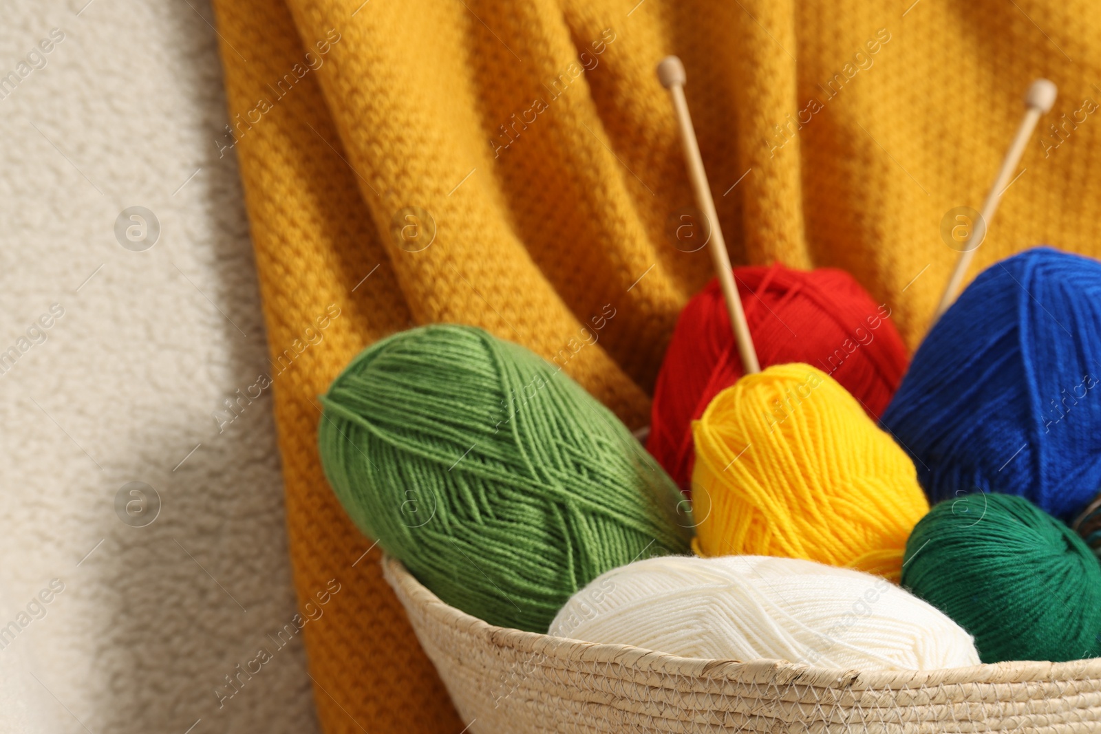 Photo of Skeins of soft yarn and knitting needles on armchair, closeup