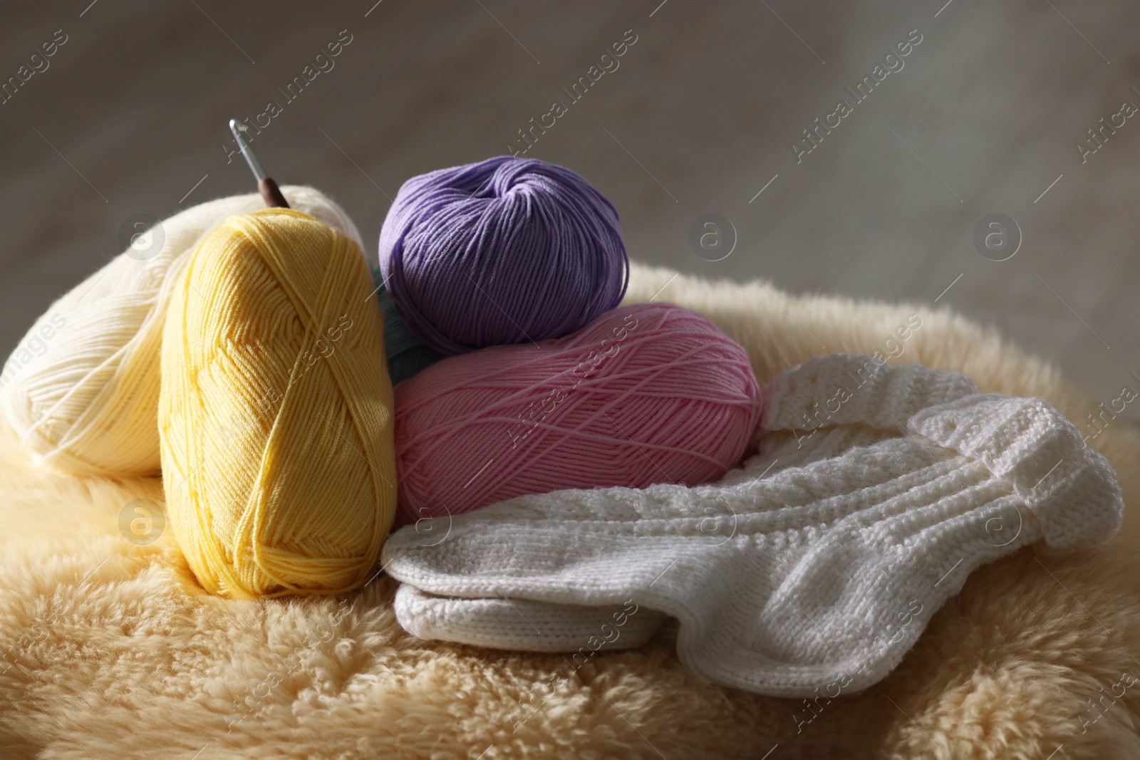 Photo of Knitting material. Skeins of yarn, crochet hook and socks on soft surface indoors