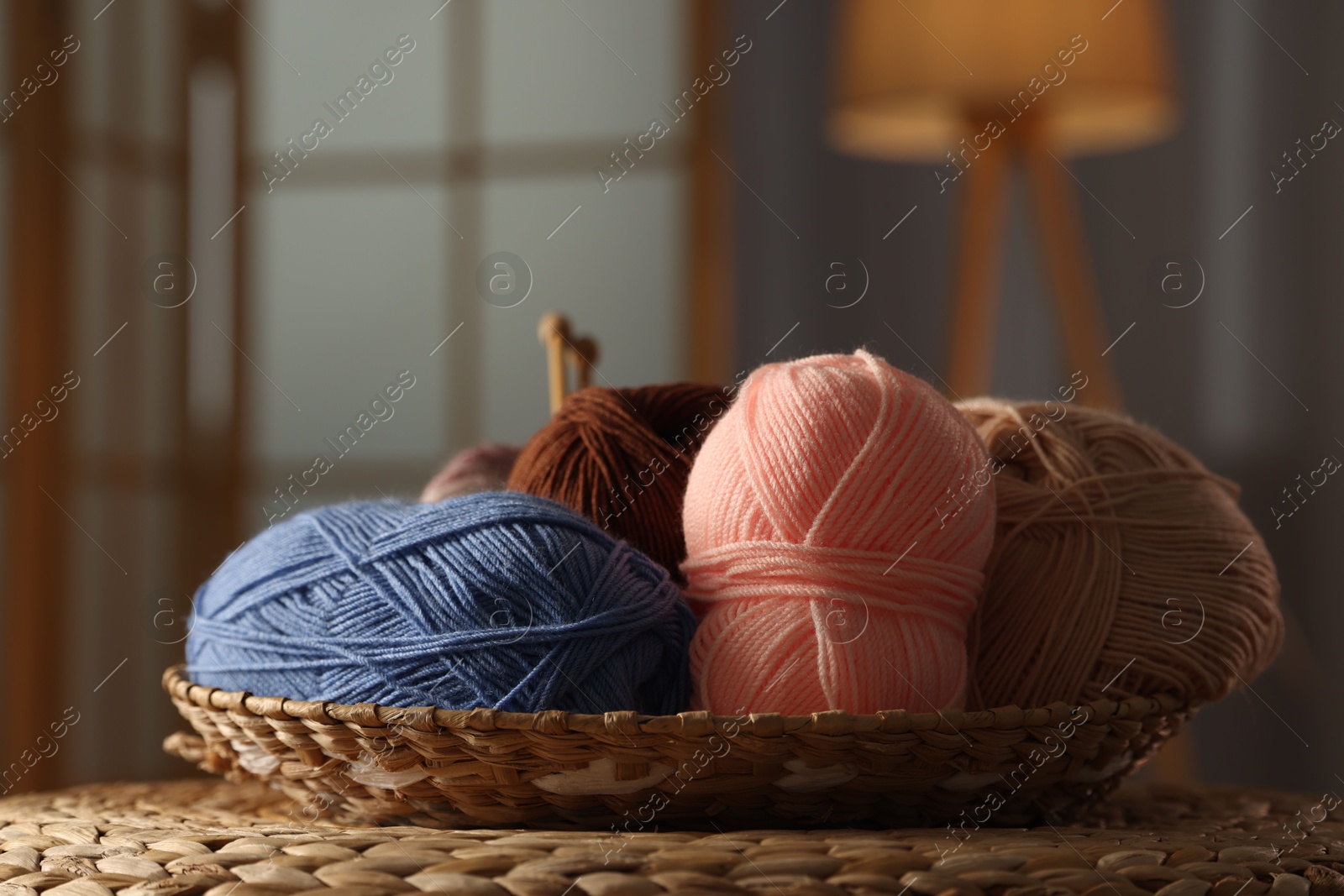 Photo of Knitting material. Skeins of soft yarn in wicker bowl on table indoors, closeup