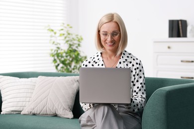 Photo of Smiling middle aged woman working with laptop on sofa at home