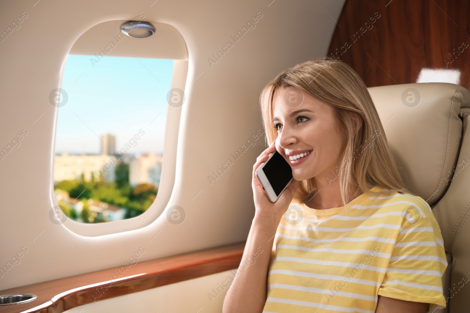 Image of Woman talking on phone in cabin while airplane taking off or landing, view on city from window