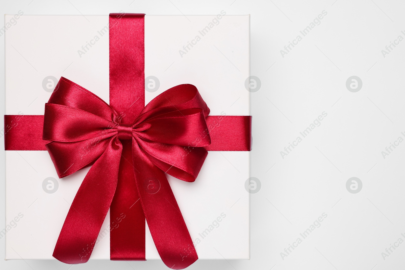 Photo of Gift box with red bow on light grey background, top view. Space for text