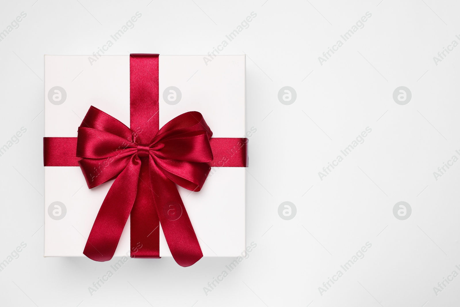 Photo of Gift box with red bow on light grey background, top view. Space for text