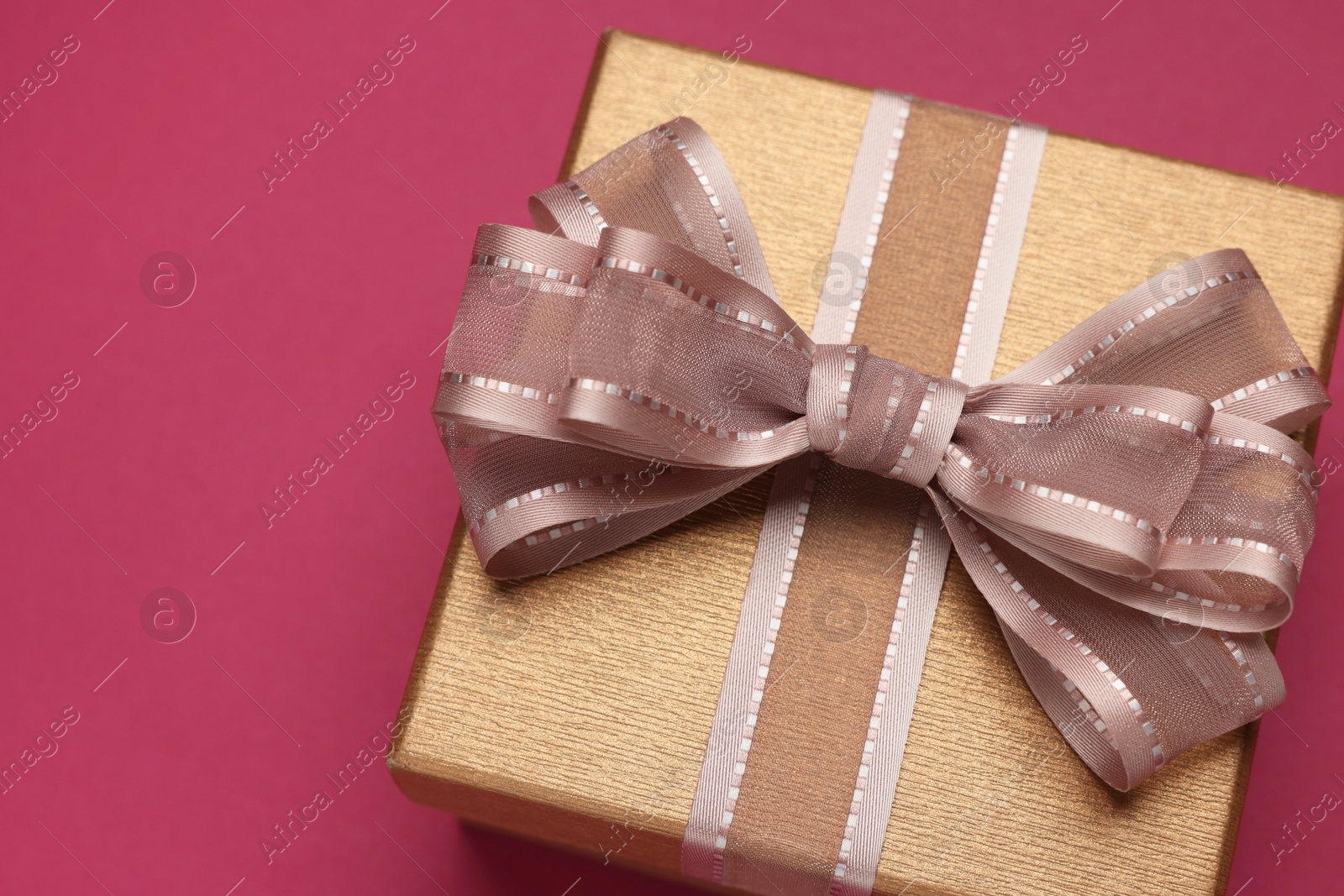 Photo of Gift box with bow on burgundy background, above view