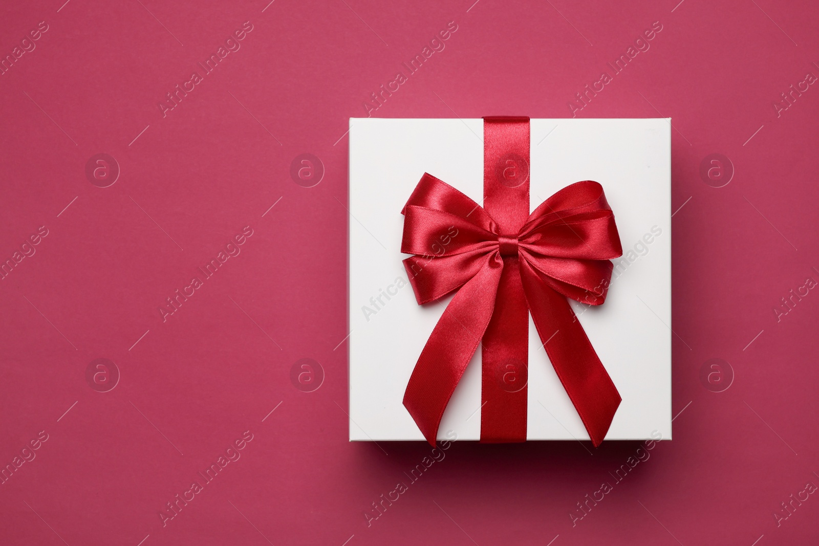 Photo of Gift box with red bow on burgundy background, top view. Space for text