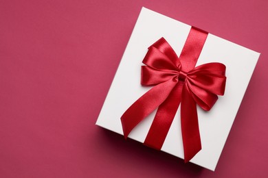 Photo of Gift box with red bow on burgundy background, top view. Space for text