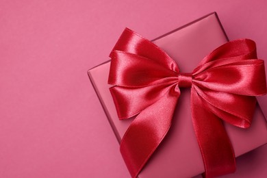 Photo of Gift box with bow on pink background, top view. Space for text