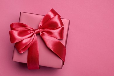 Gift box with bow on pink background, top view. Space for text