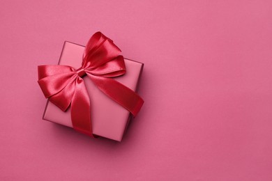 Photo of Gift box with bow on pink background, top view. Space for text