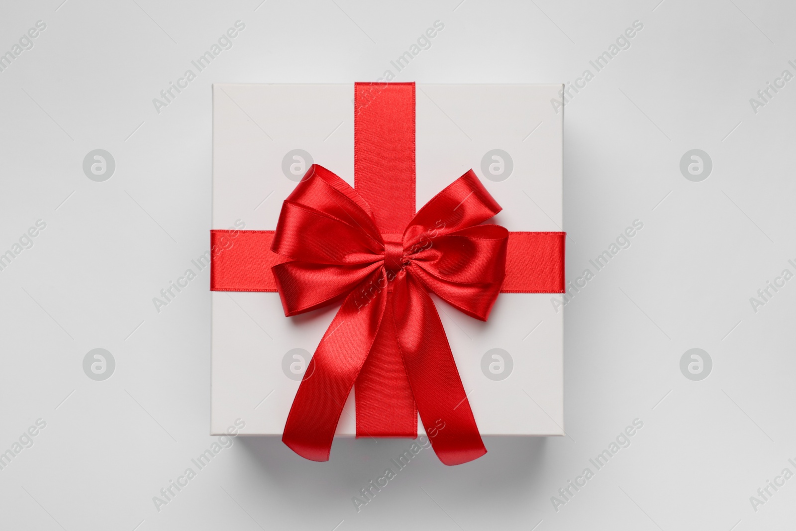 Photo of Gift box with red bow on light grey background, top view