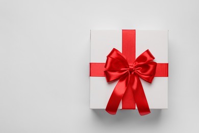 Photo of Gift box with red bow on light grey background, top view. Space for text