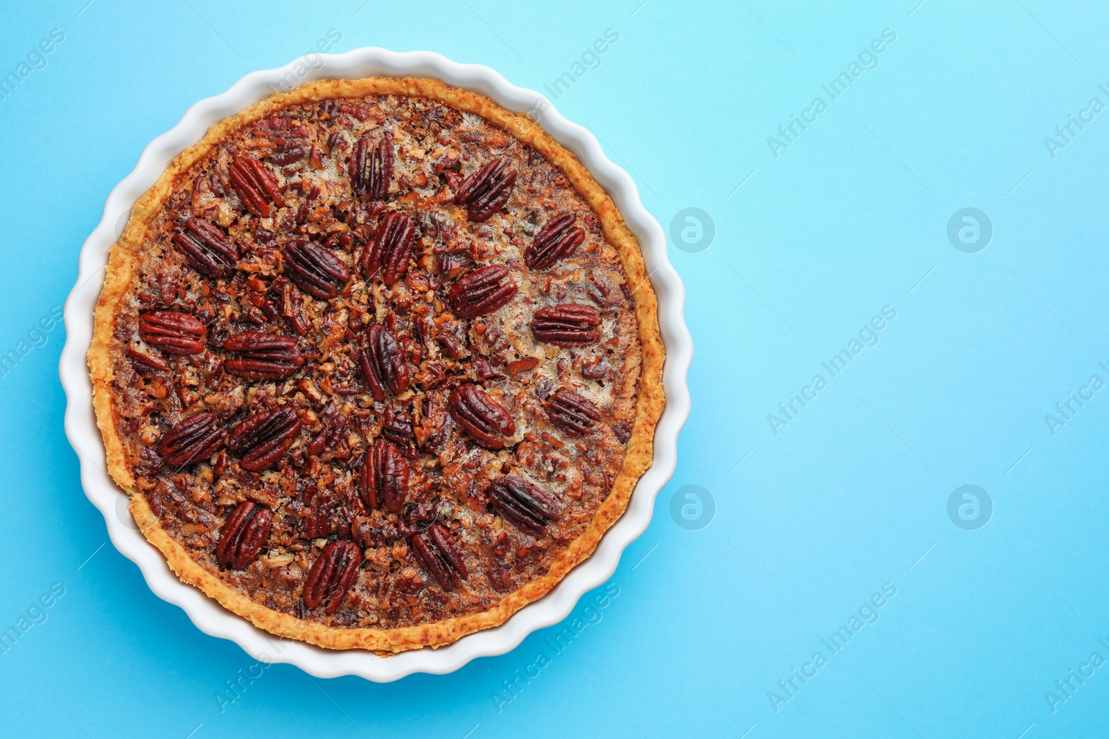 Photo of Delicious pecan pie in baking dish on light blue background, top view. Space for text