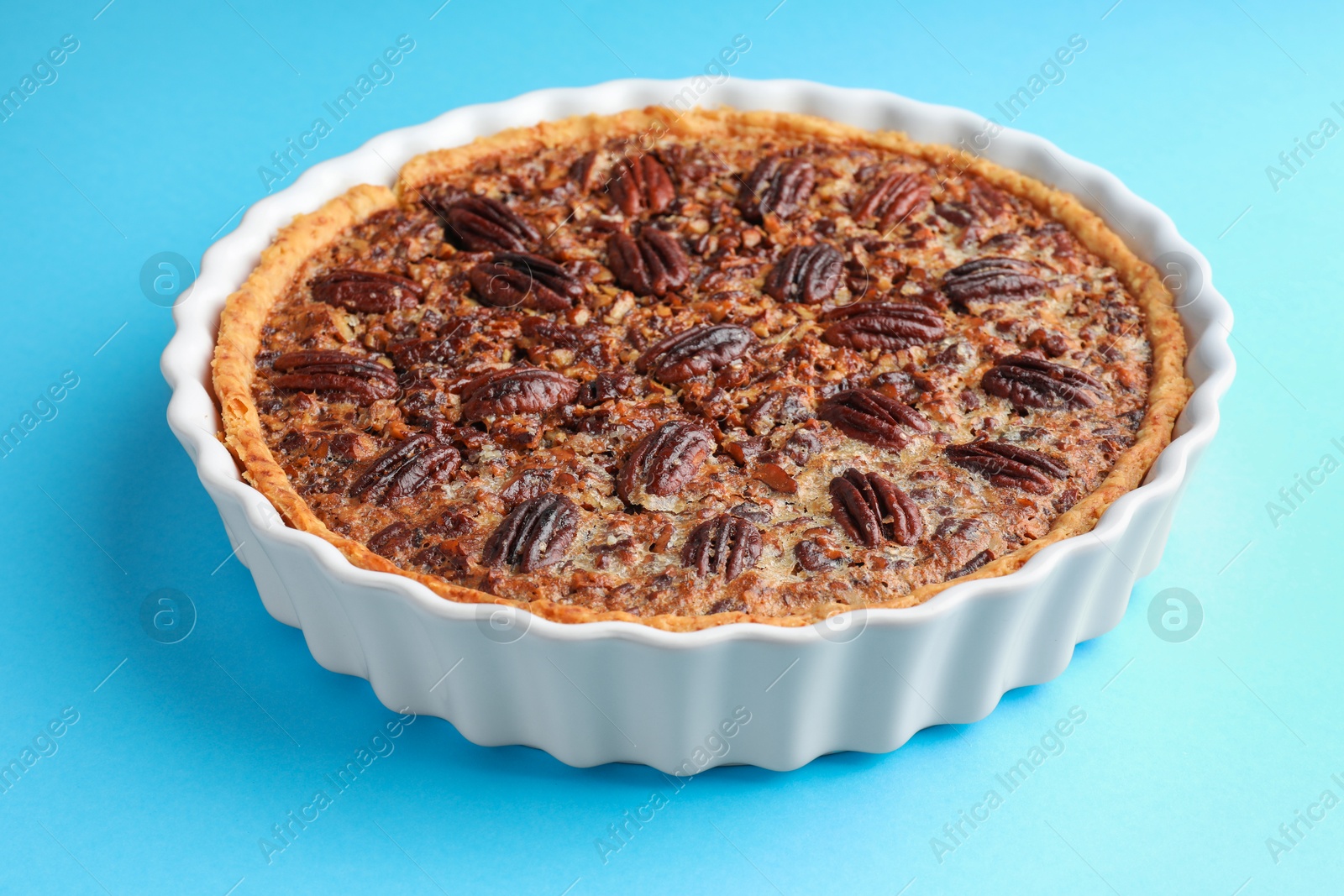 Photo of Delicious pecan pie in baking dish on light blue background, closeup