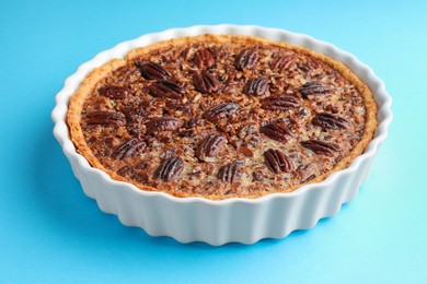 Delicious pecan pie in baking dish on light blue background, closeup