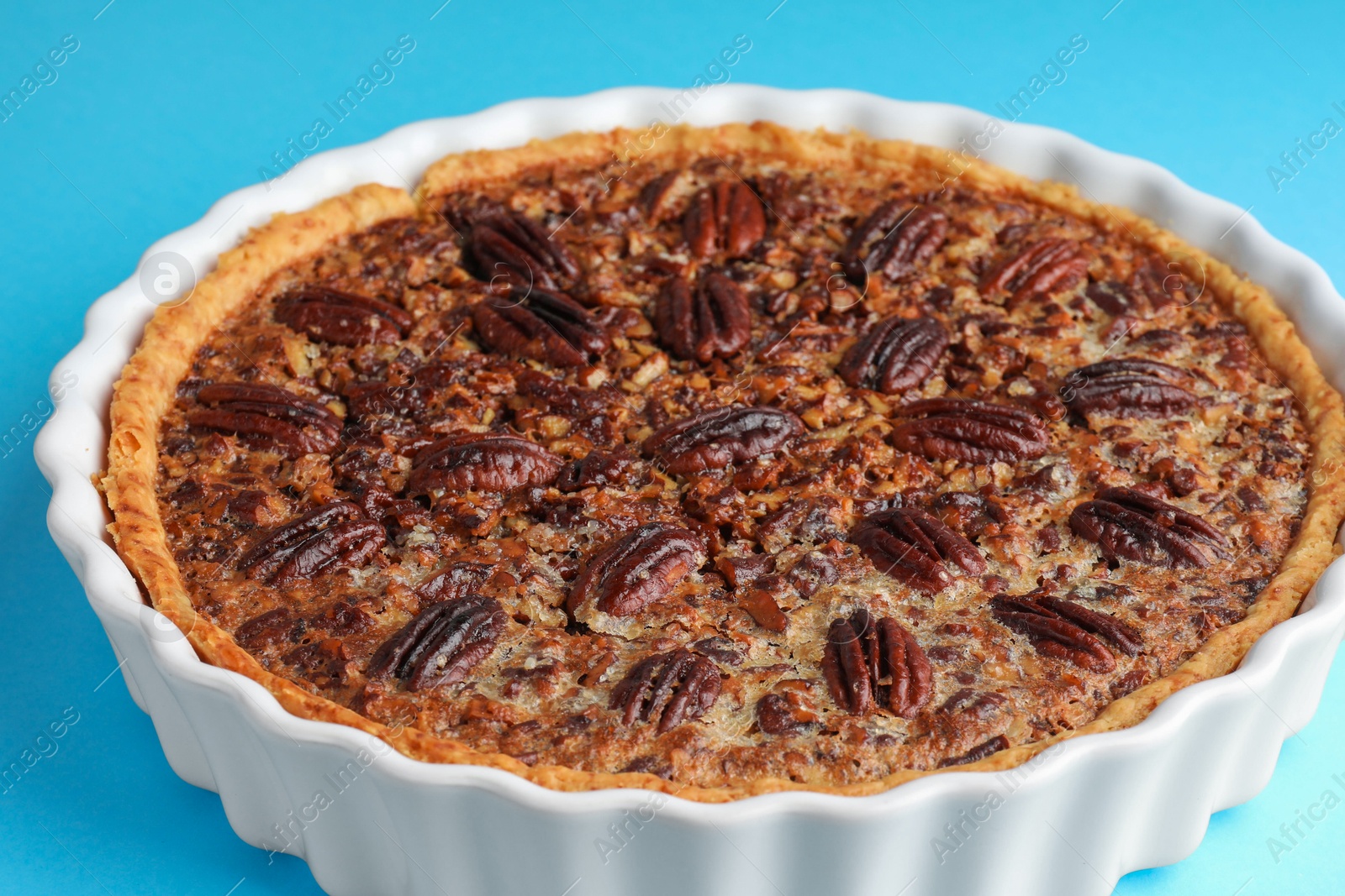 Photo of Delicious pecan pie in baking dish on light blue background, closeup