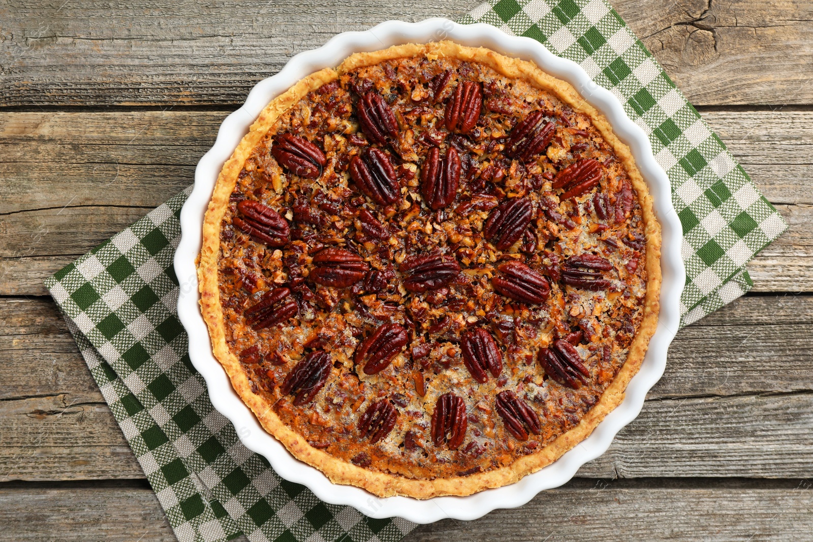 Photo of Delicious pecan pie in baking dish on wooden table, top view.