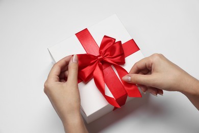 Photo of Woman decorating gift box with bow on white background, closeup