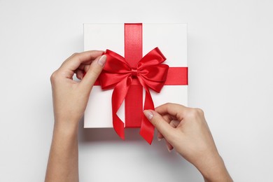 Woman decorating gift box with bow on white background, top view