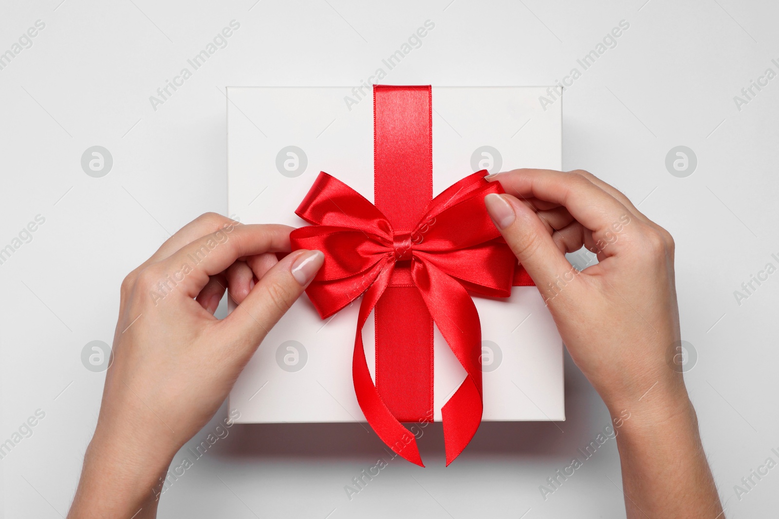 Photo of Woman decorating gift box with bow on white background, top view