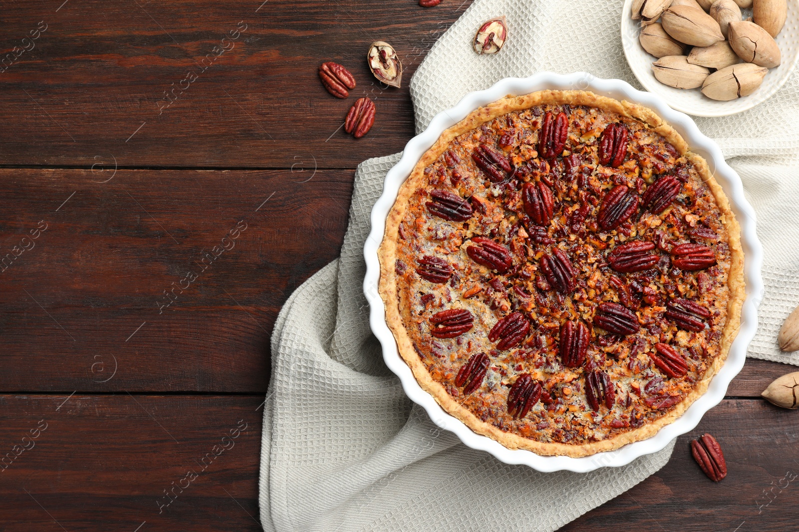 Photo of Delicious pecan pie in baking dish and fresh nuts on wooden table, flat lay. Space for text