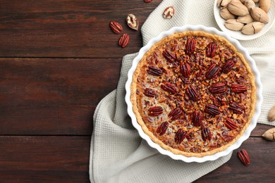 Photo of Delicious pecan pie in baking dish and fresh nuts on wooden table, flat lay. Space for text