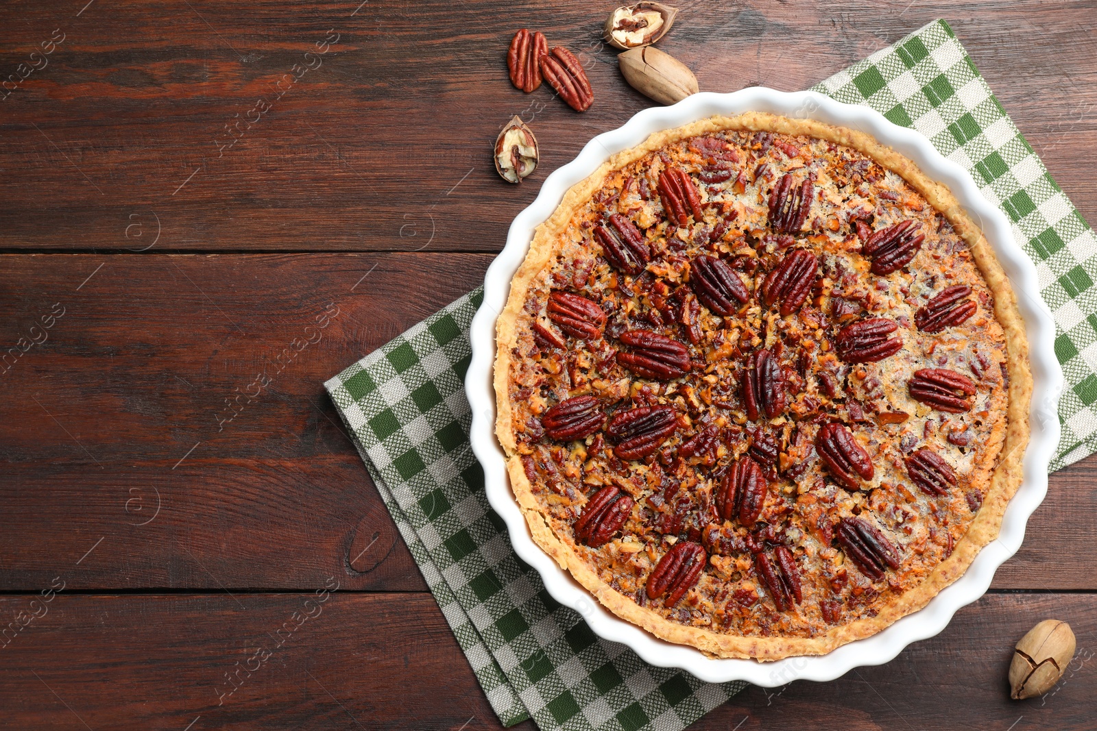 Photo of Delicious pecan pie in baking dish and fresh nuts on wooden table, top view. Space for text