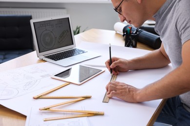 Photo of Architect making engineering drawing at wooden table in office