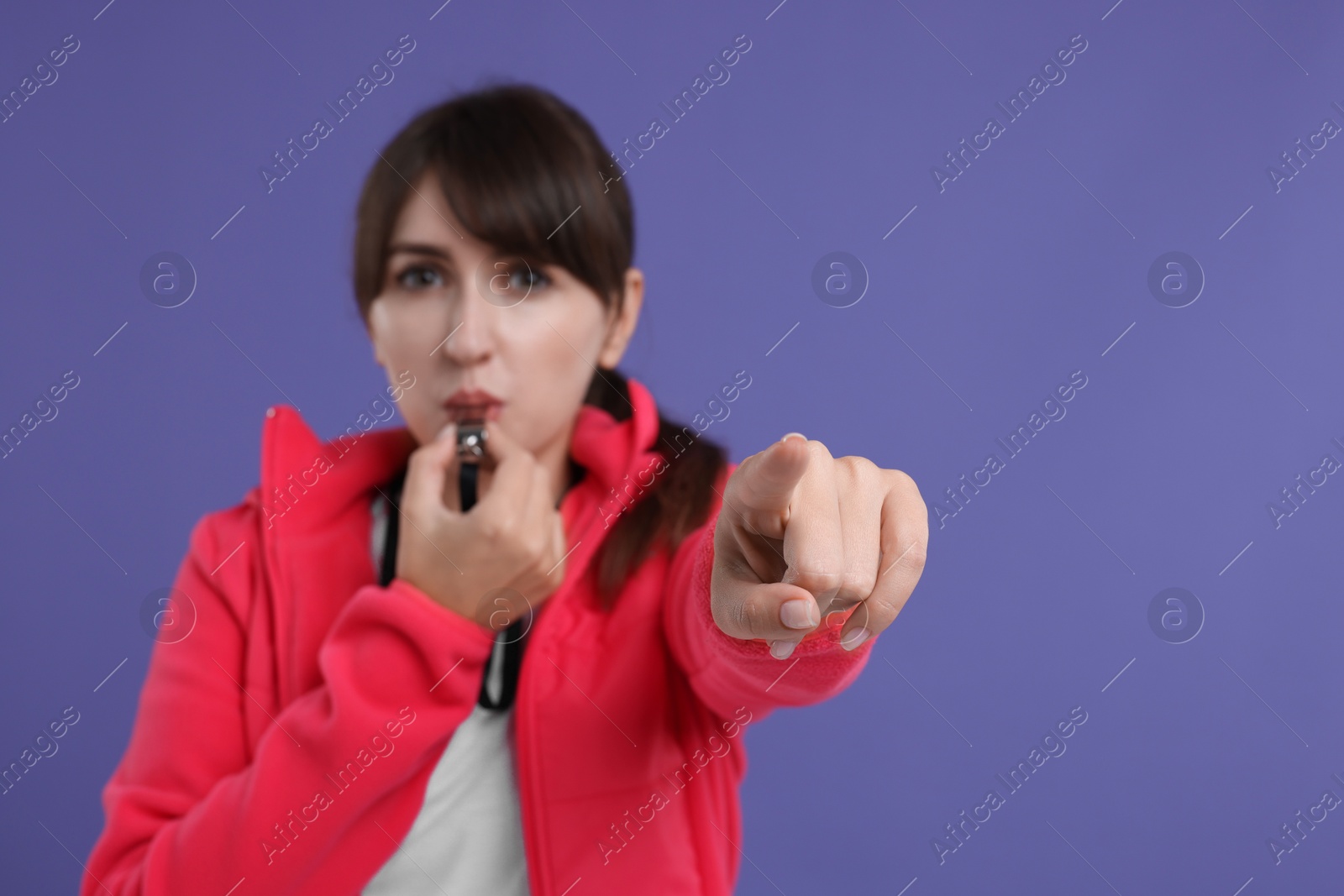 Photo of Woman blowing whistle on purple background, selective focus. Space for text