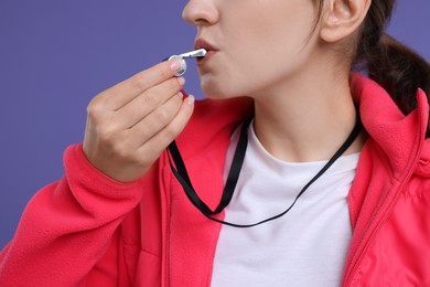 Woman blowing whistle on purple background, closeup