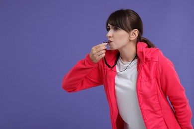 Woman blowing whistle on purple background, space for text