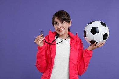 Happy woman with whistle and soccer ball on purple background