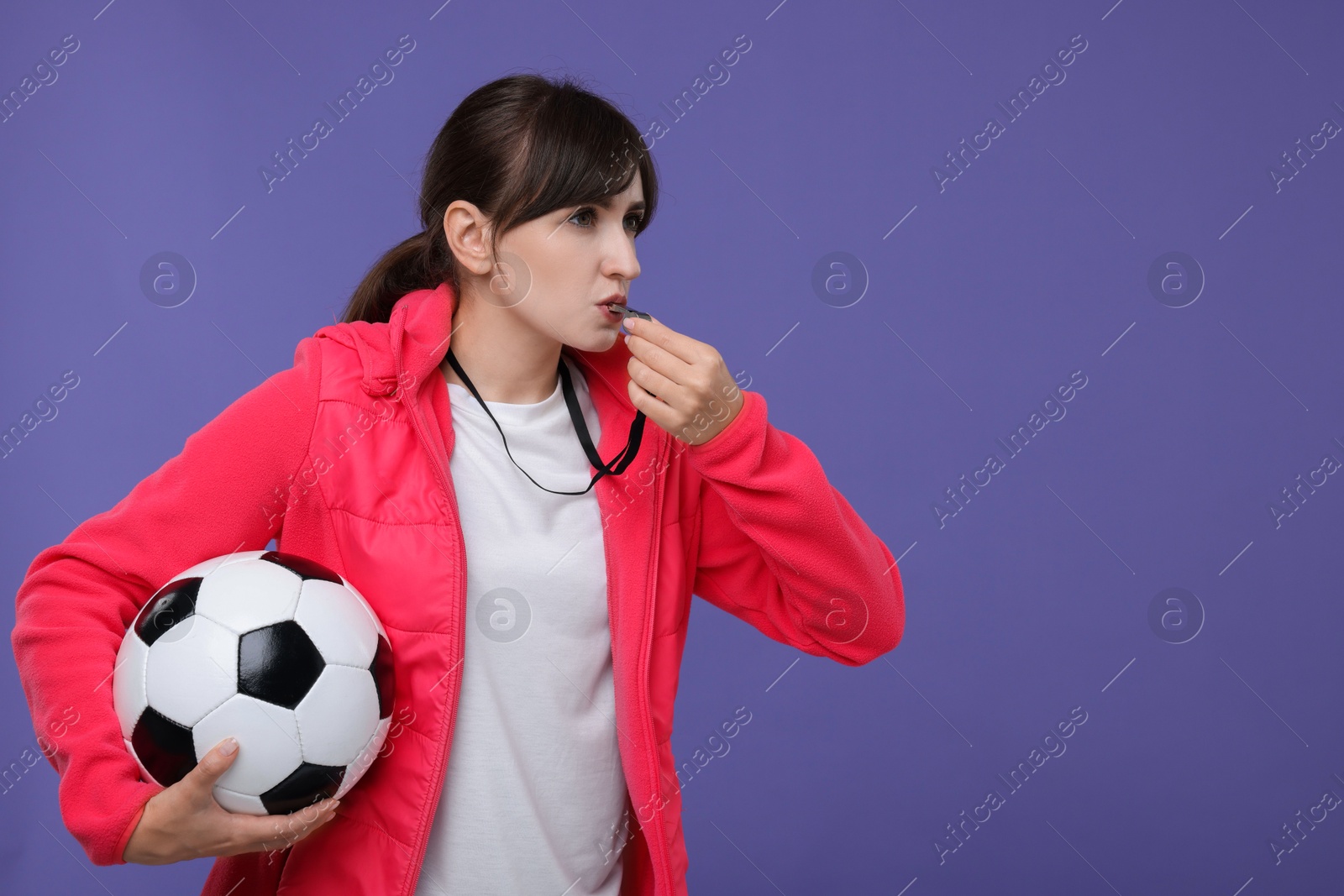 Photo of Woman with soccer ball blowing whistle on purple background, space for text