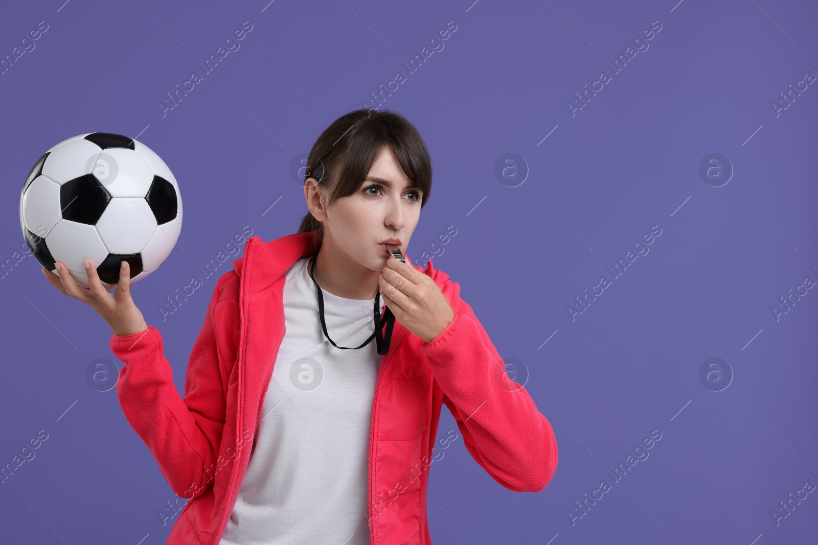 Photo of Woman with soccer ball blowing whistle on purple background, space for text